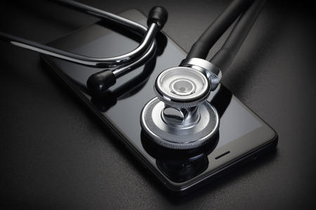 Stethoscope and smartphone on black background. Phone repair or online medical diagnosis results conceptの写真素材