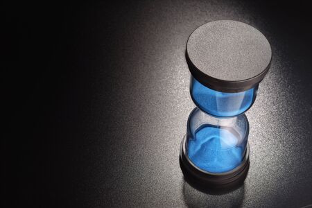 Hourglasses with blue sand measuring passage of time on black background