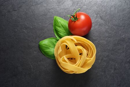 Fettuccine pasta with basil leaves and tomato on black slate background with copy spaceの写真素材