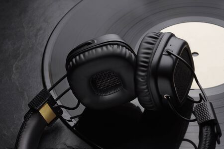 Over or on-ear headphones on vinyl record. Black background. Close-up shot