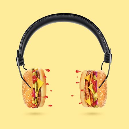 Tasty and juicy hamburger concept. Classic black headphones with burgers as a dynamics and droplets of ketchup as a sound on yellow background.の写真素材