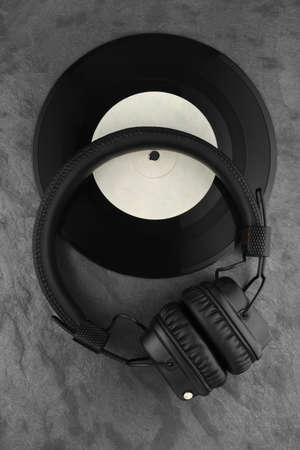 Headphones on 7-inch single vinyl record. Black slate background.