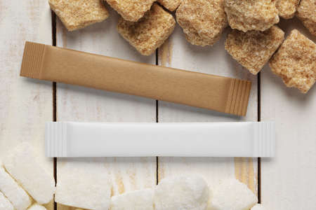 Blank brown and white paper sachet sticks and sugar cubes on wood plank tabletop. 3D rendering and...