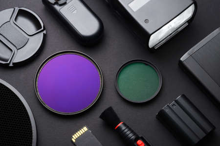 Top view of work space photographer with flash, cleaning brush, memory card, lens filters, cap, accessory on black table background.の写真素材
