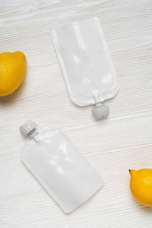 White empty plastic pouches for baby food, fruit puree on wood table. Mock-up template for design....