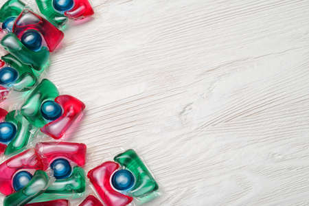 Pile of washing gel capsule pods with laundry detergent on white wooden table.の写真素材