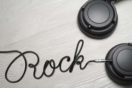 Headphones with Rock word shaped wire on the white wooden table. Music genre concept.