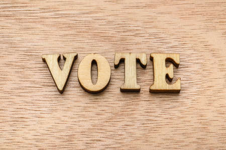 Set of wooden letter spelling the word VOTE on wooden background.