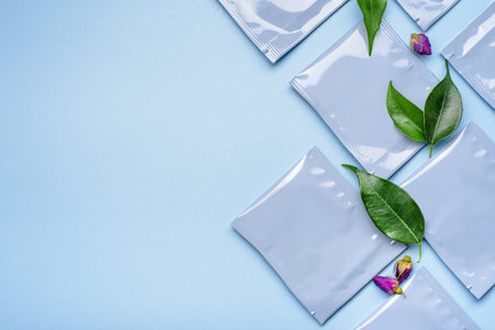 Blue plastic tea bag sachets or envelopes with dry rosebud and green leaves. Top view, copy space.