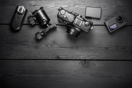 Digital compact and action cameras and equipment on black wooden plank table. Top view, flat lay,...
