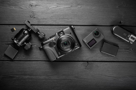 Digital compact and action cameras and photographic equipment on black wooden plank table. Top view,...
