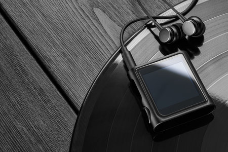 Portable digital music player on vinyl record with headphones on dark black wooden surface.