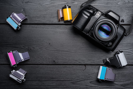 A vintage camera with colorful film rolls arranged on a rustic wooden table, showcasing the art of photography and film development.の写真素材