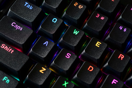 Close-up view of a black gaming keyboard with the Tab, Caps-Lock and Shift keys highlighted by bright RGB backlight.の写真素材