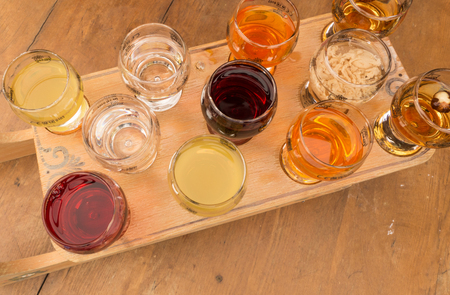 A group of glasses of various alcohol stacked on wooden boardの写真素材