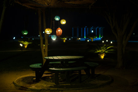 wooden table with seats placed in garden below red, yellow, green and red color lights and wooden...