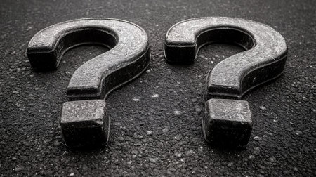 Two large, black question marks sit on a textured surface.の素材