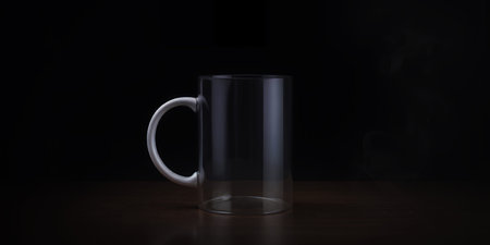 An empty clear glass mug with a white handle sits on a dark wooden surface. Clear details and vibr...の素材