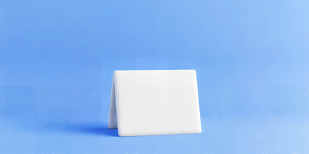 A white blank folded card stands on a blue textured background. Clear details and vibrant colors e...の素材