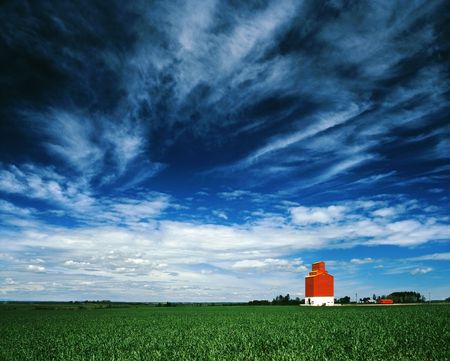 Grain elevator sits on the Canadian prairies with big blue sky overhead and green wheat field in foreground.の写真素材