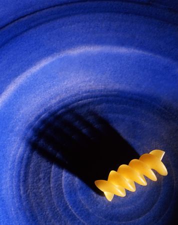 Single piece of rotini pasta sits on a blue plate casting an interesting  shawdow.の写真素材