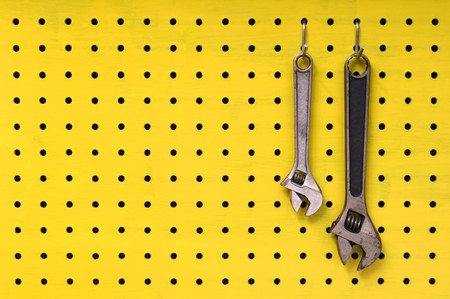 Pair of metal wrenches hang together off of hooks on yellow pegboard.の写真素材