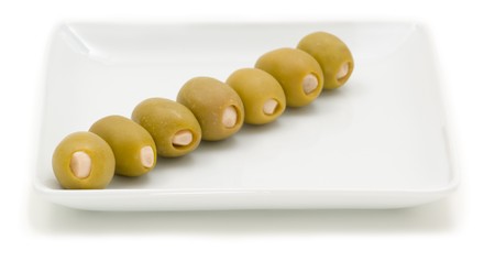 Garlic-stuffed olives sit in a diagonal line on a white dish.の写真素材