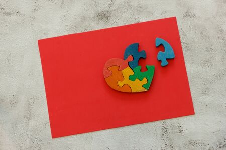 Wooden multicolor puzzle in the form of heart with disconnected piece on a red sheet on gray backgroundの写真素材