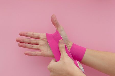 Hand with violet kinesiology tape isolated on pink background. Physiotherapy and therapeutic tape for wrist pain, aches and tension. elastic therapeutic tape. adhesive tape and alternative medicine.の写真素材