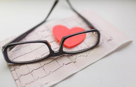 Cardiogram chart with glasses and red heart on table closeup. Cardiovascular Disease Prevention