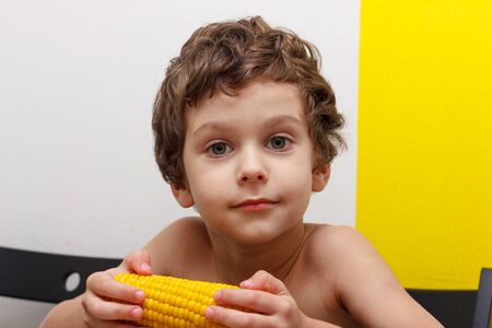 lovely curly boy eat a cob of boiled corn, GMO free.の写真素材