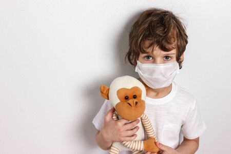 Portrait of kid wearing medical mask with toy monkey on white background. Concept of coronavirus quarantine or covid-19.Protection against virus and infection control concept.の写真素材