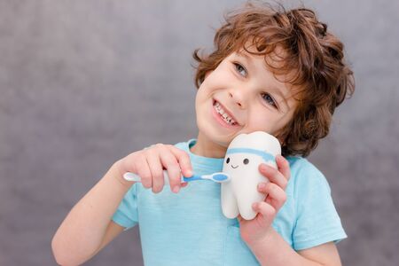 Charming curly boy smiles without tooth on gray background. The boy lost the first milk tooth. Healthy teeth concept, dental clinic.の写真素材