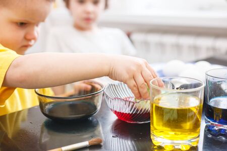boy dips an egg in a glass with paint. Boy paints easter eggsの写真素材