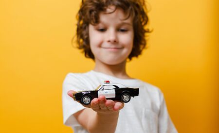 Child boy is holding a toy police car in white tshirt in yellow background. Closeupの写真素材