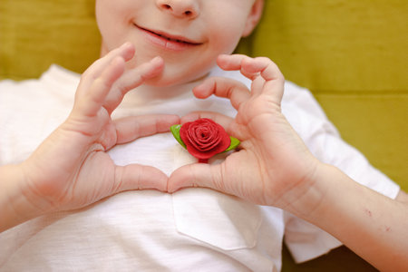 Boy in White tshirt making heart symbol with hands with red roseの写真素材