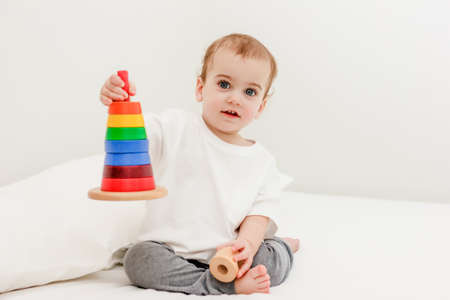 Cute baby boy playing colorful pyramid tower on white bed