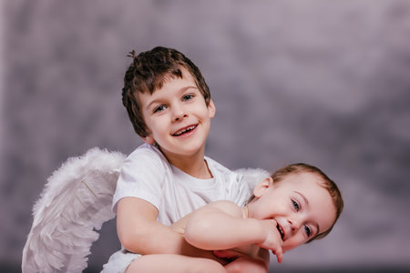 boy wearing angel wings embraces a small childの写真素材