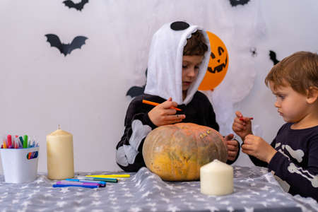 Children in Halloween costumes paint pumpkins. Boy decorate the house for holiday. Celebrating at home concept.の写真素材