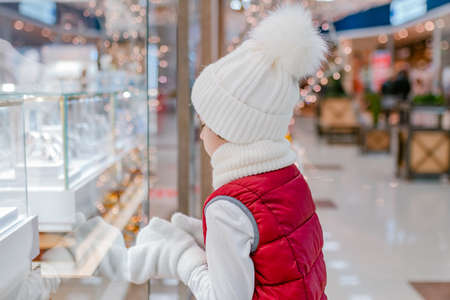 Boys in white fluffy hat looks into the store through the window and points something ih showcase in market.の写真素材
