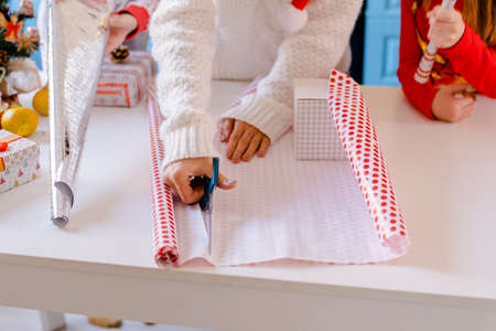 Cropped Woman packs Christmas gifts, cuts packing paper with scissors
