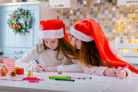 Children in Santa hats write a letter to Santa Claus in the Christmas decorated kitchenの写真素材