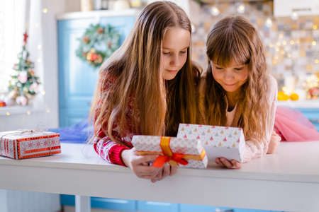 two girls are sitting in the kitchen and shaking boxes with giftsの写真素材