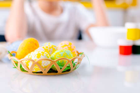 Close-up colored Easter eggs in little basket paints and kids hands on background.