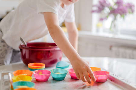 Little kid 5 years old cooks cupcakes in light kitchen at home. Little boy uses silicone baking moldsの写真素材