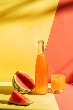 watermelon juice in bottle and watermelon slice on yellow and red backgroundの素材