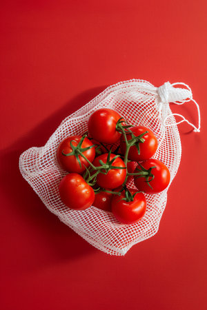 Cherry tomatoes in a reusable mesh bag on a red background.の素材