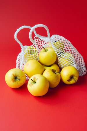 Ripe yellow apples in a string bag on a red background.の素材