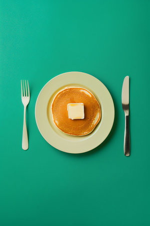 Pancake with butter on a green plate with fork and knifeの素材