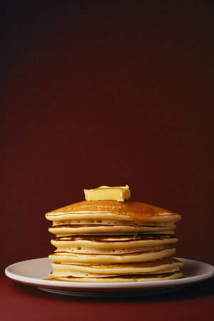 Stack of pancakes with butter on a plate on a dark red backgroundの素材